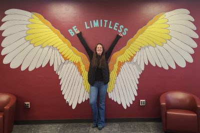 Hannah Pratt standing in front of a winged mural.